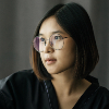 Woman wearing a black coat, wearing glasses, sitting, pressing the remote control to turn on the air.